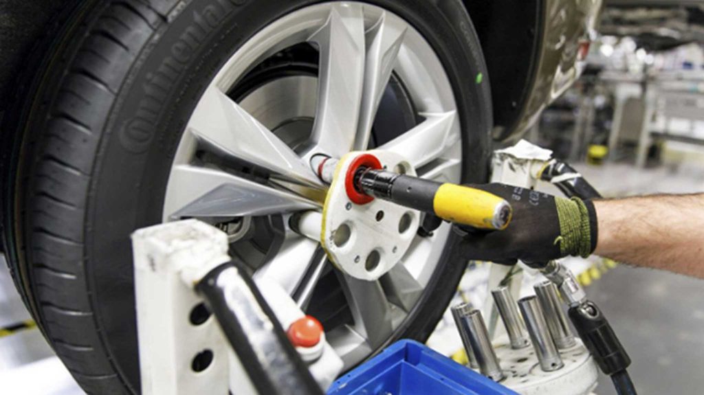 Uma mão com luva de borracha preta está utilizando um equipamento para fazer reparos em uma roda de automóvel.